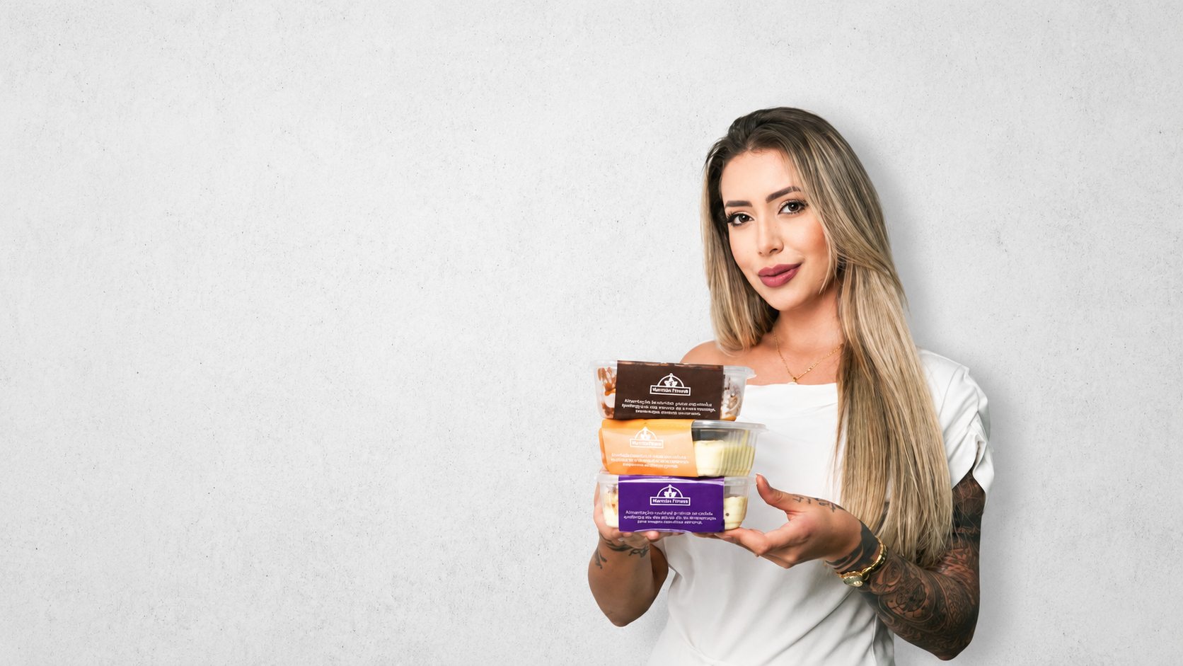 Dona da Delícias Fitness segurando marmitas fitness com tampas coloridas